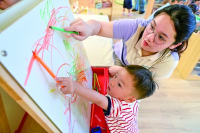 在江苏省南京一家托育中心,一名小朋友在托育老师的陪伴下画画。新华社发
