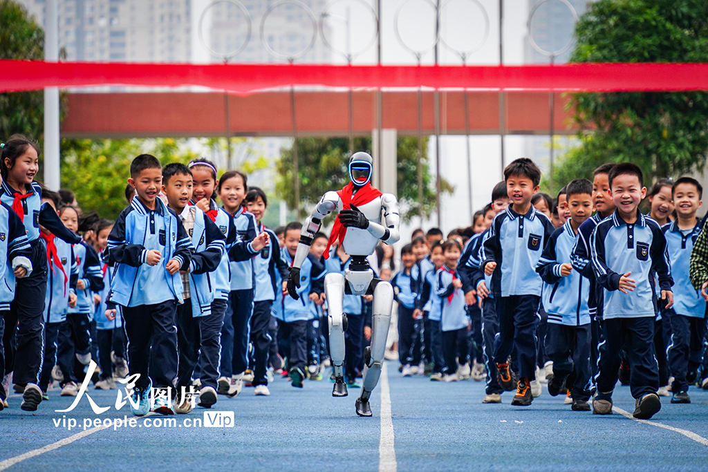 2026年3月2日，广西南宁天桃实验学校青运校区开展“开学第一跑”活动，学生们与人形机器人在操场上快乐奔跑，在互动体验中激发了对科学的探索兴趣。叶子榕摄（人民图片网）